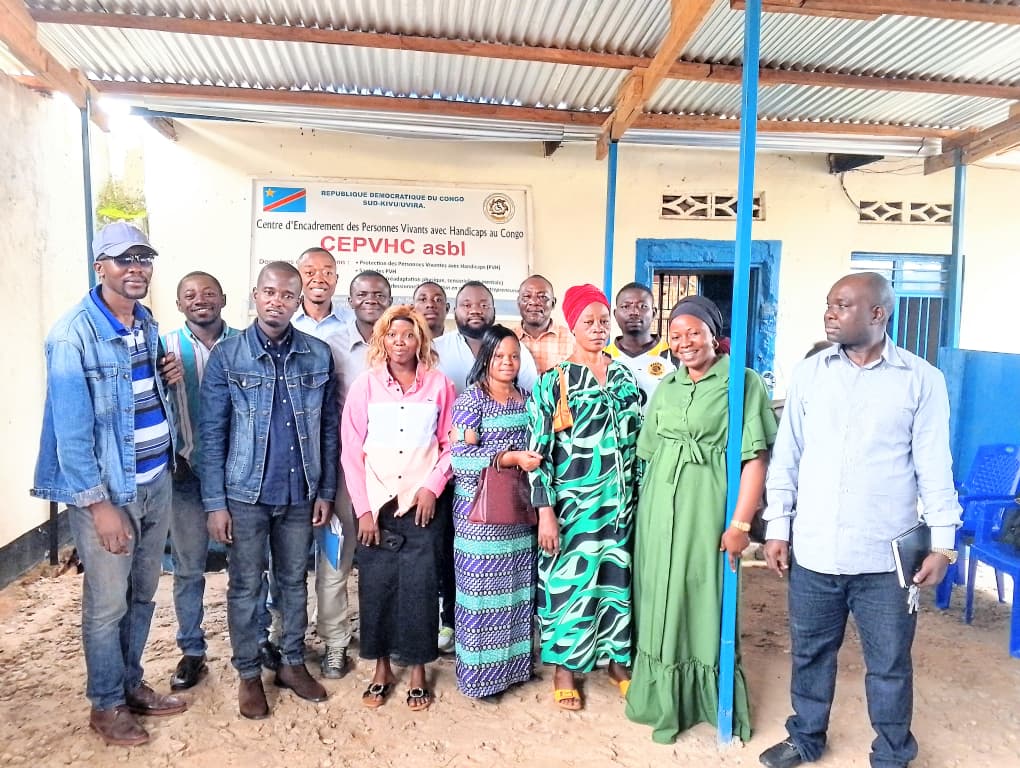 Groupe de personnes composant l'équipe et les membres du Centre d’Encadrement des Personnes Vivant avec Handicaps au Congo (CEPVHC) posant devant le bâtiment du siège affichant la signalétique officielle de l'ONG.