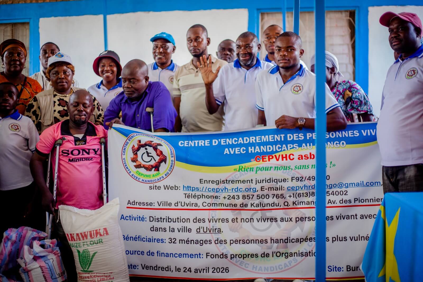 Groupe de bénéficiaires et membres du CEPVHC asbl posant devant des sacs de farine de maïs Akawuka lors d'une activité de distribution de vivres en intérieur.