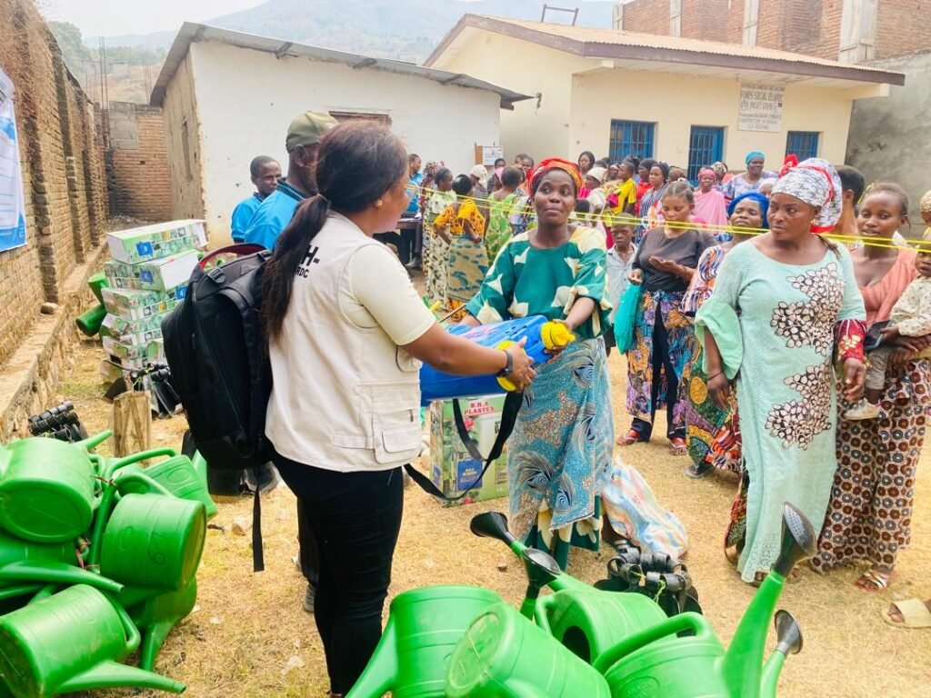 Une agente du CEPVHC remet un pulvérisateur à une femme bénéficiaire à Kilomoni (Uvira), avec des arrosoirs au premier plan.